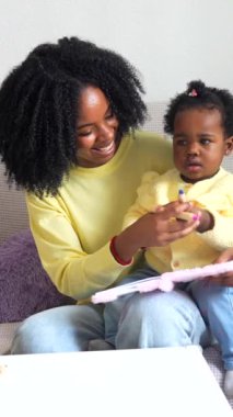 Afrikalı anne ve çocuk oturma odasındaki kanepede oturarak resim çiziyor.