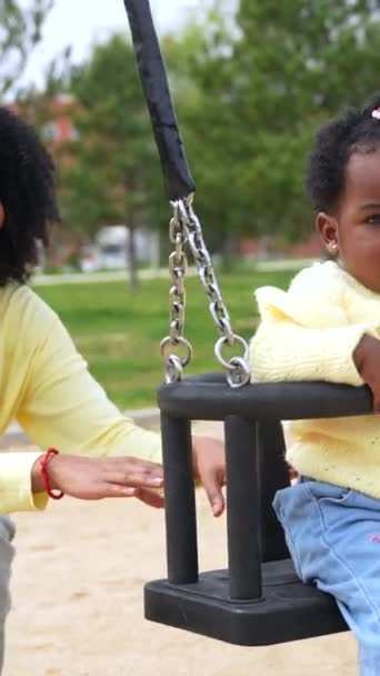 微笑着的非洲母亲推着女儿在公园里荡秋千 免版税图库视频