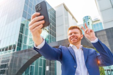 İş adamı şehirde selfie çekerken başarılı bir jest yapıyor.