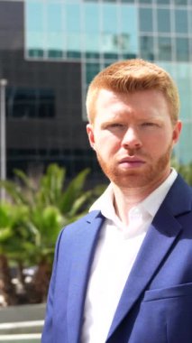 Gururlu iş adamı güneşin altında kollarını kavuşturarak finansal yapı cephesine dayanıyor.