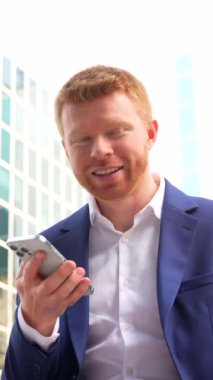 Bir iş adamının açık havada cep telefonuyla konuşurken yan yana baktığı dikey video.