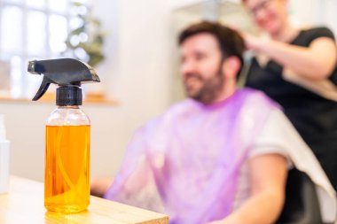 Flask with water to spray the hair of clients in the salon with a man with wing sitting on the background clipart
