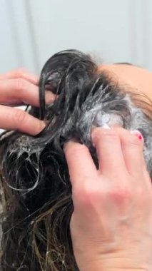 Kuaförün ellerinin yakın plan fotoğrafı. Hasarlı bir kadının saçını yıkıyor.