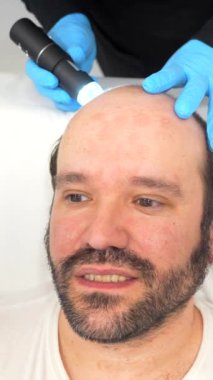 Dermatolog, güzellik kliniğinde kel bir hastaya prosedürü açıklamak için bir ekran kullanıyor.