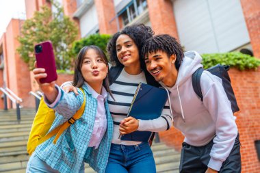 Senin düşük açılı portren, çok ırklı havalı üniversite öğrencilerinin kampüste selfie çekerken.