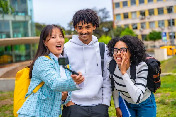 Kolme Siistiä Monietnistä Opiskelijaa Puhuu Selfiestä Puettavan Kameran Jalustan Kanssa kuvapankkikuva