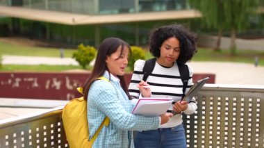 İki güzel, genç, gülümseyen çoklu etnik öğrenci üniversite kampüsünün dışında duran notları okuyorlar.