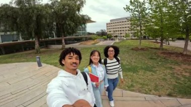 Üniversite kolajının dışındaki video çağrısında el sallayan üç çok ırklı öğrenci