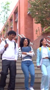 Üç çok ırklı kadın ve erkek öğrenci üniversitenin dışında eğleniyor ve dans ediyor.