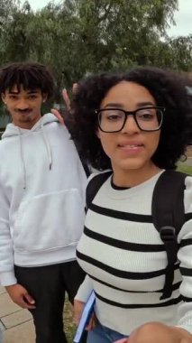 Üç çok ırklı öğrenci kampüsün dışında takılabilir bir kamerayla bir video kaydederken el sallıyor.