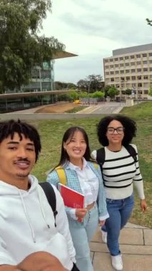 Üniversite kolajının dışındaki video çağrısında el sallayan üç çok ırklı öğrenci