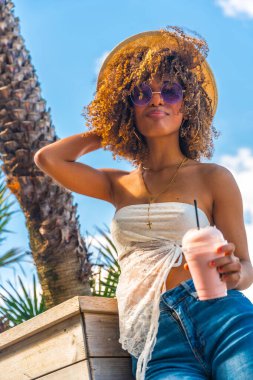 Vertical low angle view of a cool latin woman enjoying summer drinking milkshake next to palm tree