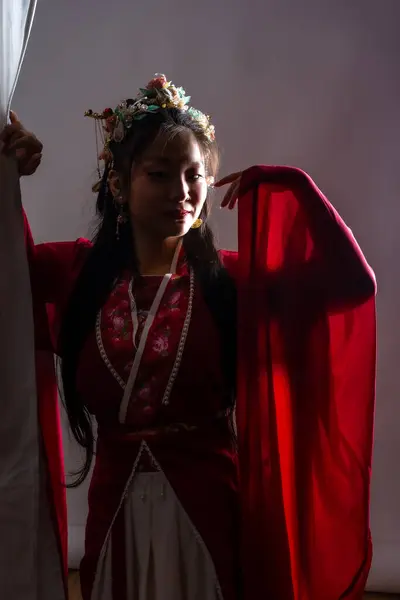 stock image A woman in a red dress with a flowery headpiece. She is standing in front of a white curtain