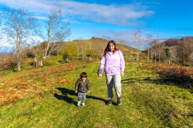 Bir kadın ve bir çocuk çimen tarlasında yürüyorlar. Kadın mor bir kapüşonlu giyiyor.