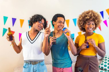 Mutlu çok ırklı arkadaşlar oturma odasında karaoke yapıyor. Duvarında renkli çelenkler var.
