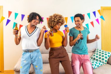 Çeyrek boyunda bir grup kadın ve erkek çok ırklı arkadaşın evde karaoke yapıp dans ettiği bir fotoğraf.