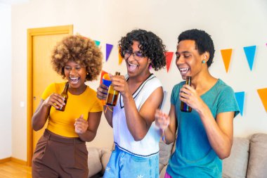 Çok ırklı arkadaşlar parti sırasında evde mutlu bir şekilde karaoke söyleyip dans ediyorlar.
