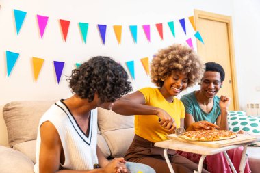 Afrikalı kadın, çok ırklı erkek arkadaşlarıyla paylaşmak için pizzayı dilimlere ayırıyor.