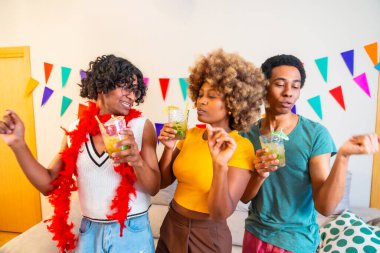 Çok ırklı arkadaşlar evde dans edip kokteyl içiyorlar.