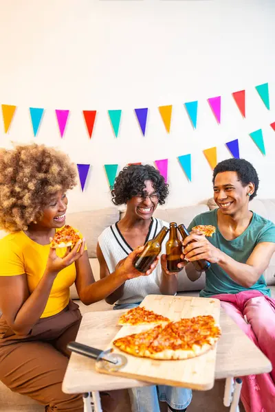 Üç farklı erkek ve kadın arkadaşın evdeki kanepede oturup pizza yerken çekilmiş dikey fotoğrafı.