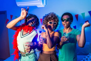 Çok ırklı mutlu arkadaşlar gece partisinde evde dans edip içiyorlar.