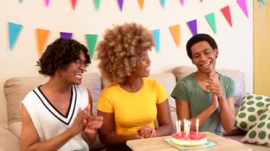 Üç çok ırklı erkek ve kadın arkadaş evde şarkı söyleyip el ele tutuşarak doğum günü kutluyorlar.
