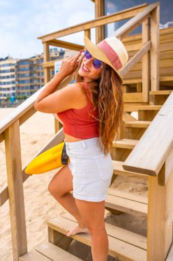 Kaliforniya sahilinde tatilin tadını çıkarırken cankurtaran kulesinde gülümseyen beyaz kadın portresi.