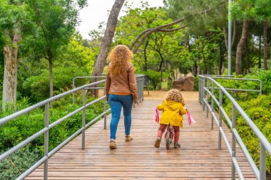 Kafkasyalı bir anne ve küçük bir kızın parkta yürümesi ve bisiklete binmesi.