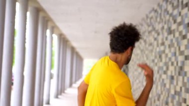 Şehirde dans eden sarı tişörtlü siyah etnik adam mavi ve beyaz fayans desenli bir duvarın önünde duruyor.