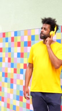 Şehirde dans eden, sarı tişörtlü, siyah etnik bir adam kulaklık takıyor ve bir şeyi işaret ediyor. Görüntünün rahat ve rahat bir havası var. Müzikten hoşlanan bir adam ya da dinlediği bir şey gibi.