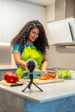 Latin kökenli genç bir kadının dikey fotoğrafı evde sağlıklı yemek dersi veriyor.