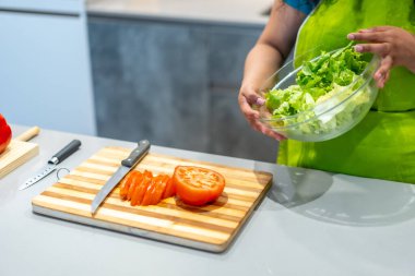 Domates kesen ve evde salata hazırlayan bir kadının yakın çekimi.