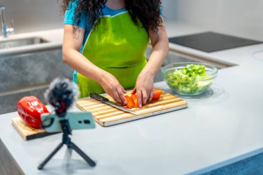Latin kökenli genç bir vlogger canlı yayın sırasında salata yapıyor.