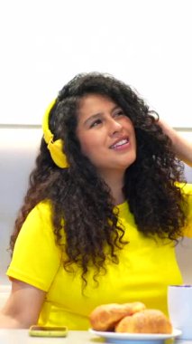 Evde kahvaltı yapan ve müzik dinleyen Latin bir kadının dikey videosu.