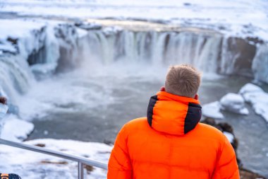 Kışın İzlanda 'daki güzel Godafoss şelalesine bakan bir adam. kış turizmi