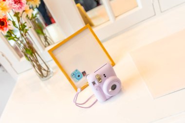 Bir fotoğraf çerçevesinin yanındaki masada mor bir kamera var. Kamera şu anda fotoğraf çekiyor ve mor renkte..