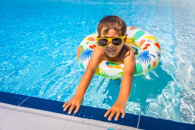 Güneş gözlüklü bir çocuğun güneşli bir günde havuzda şişme yüzüğe uzanmış tam boy fotoğrafı.