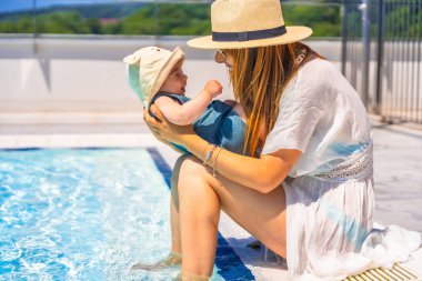 Yüzme havuzunda güneşli şapkalı bir anne ve şirin bir bebek.