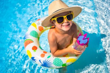 Havuzda su içen beyaz bir çocuğun kamera karşısında gülümseyen renkli bir şamandıranın üst görüntüsü.