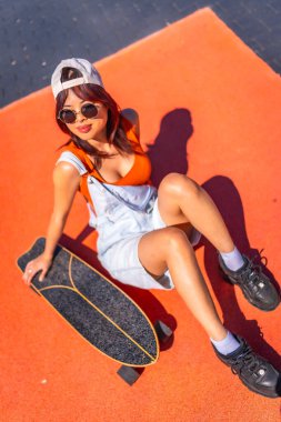 Renkli bir şehir parkında kaykayın yanında oturan kendine güvenen Çinli bir kadının dikey portresi.