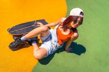 Renkli kaykay parkında oturan havalı genç bir kadının yükseliş manzaralı portresi