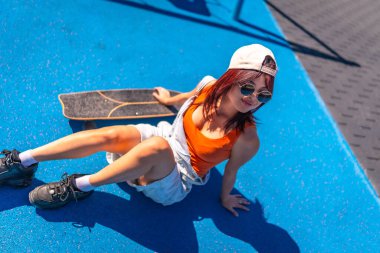 Parkta kaykayın yanında oturan kot paltolu, kafası karışmış Asyalı genç bir kadının en iyi görüntüsü.