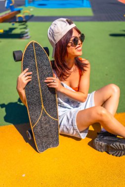 Parkta renkli zemini olan kaykaylı modern bir genç kadının dikey portresi.