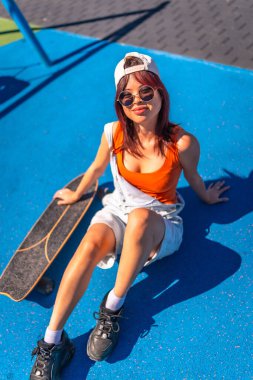 Şehirdeki renkli kaykay parkında oturan Çinli genç bir kadının dikey görüntüsü.