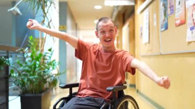Üniversitede tekerlekli sandalyede oturan ve kameraya gülümseyen engelli gururlu adam.