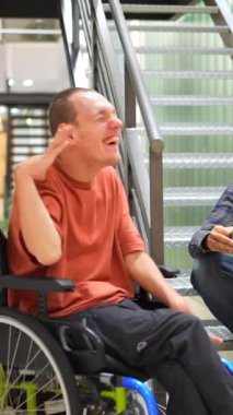 Tekerlekli sandalyedeki bir adam iş yerinde bir iş arkadaşıyla kahve içip sohbet ediyor.