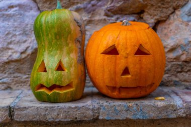 Yüzleri oyulmuş iki balkabağı bir çıkıntıya oturur. Balkabakları turuncu ve yeşil. Cadılar Bayramı temalı bir ortamda gibiler.