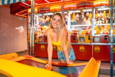 Geceleri fuarda hokey oynarken kameraya gülümseyen sarışın kadın.