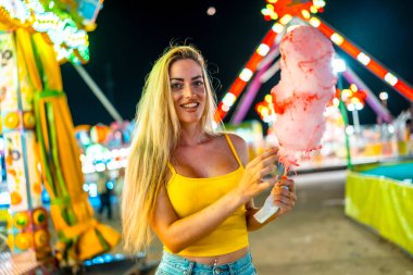 Geceleri fuarda elinde pembe pamuk şeker tutan güzel bir kadının portresi.