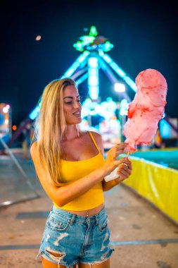 Sarışın bir kadının pamuk helva yerken çekilen dikey fotoğrafı yaz boyunca panayırda duruyordu.